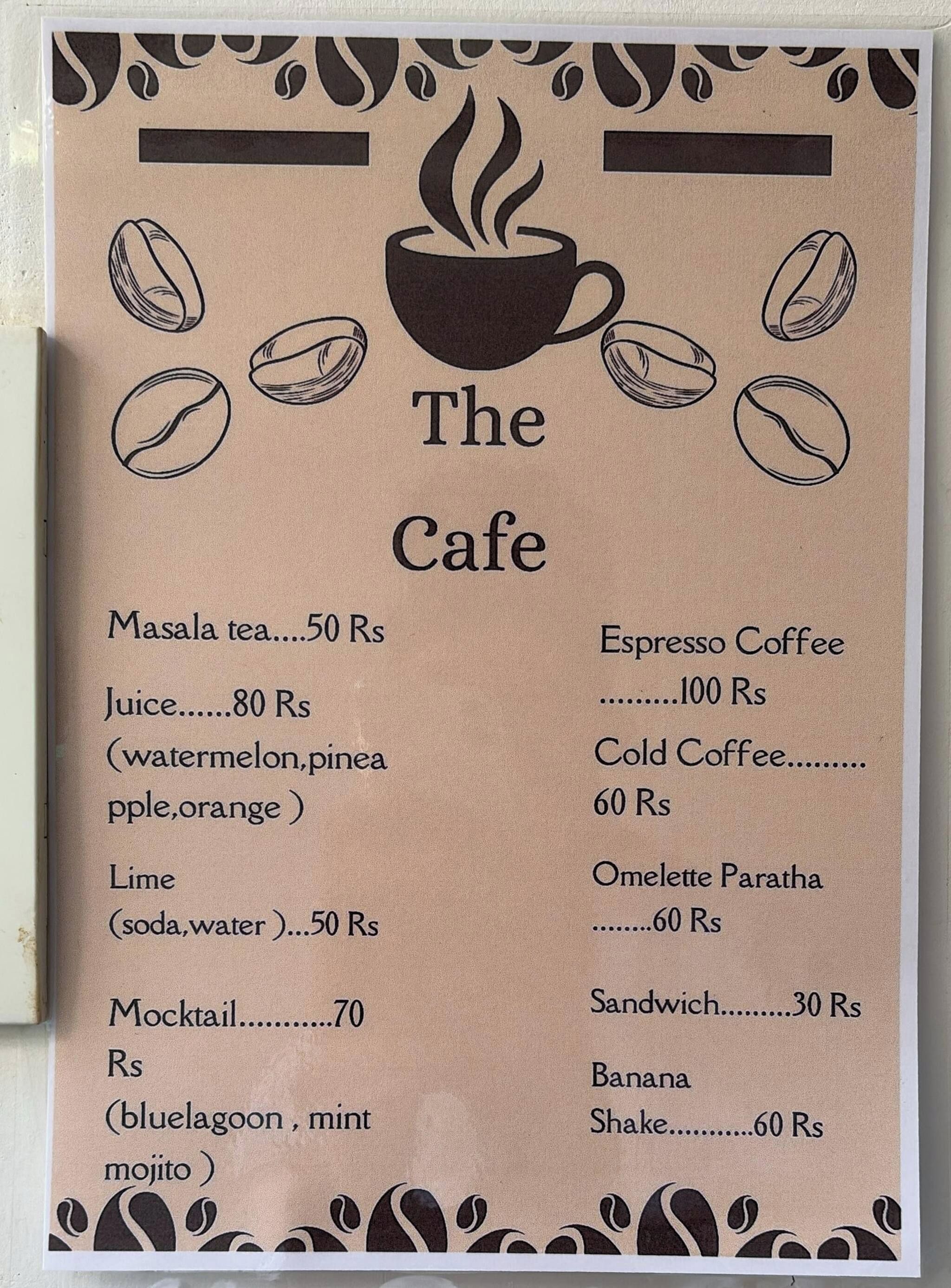 Pizarra de menú para 'The Cafe' que muestra artículos como té masala, jugo y cóctel sin alcohol, junto con sus precios.