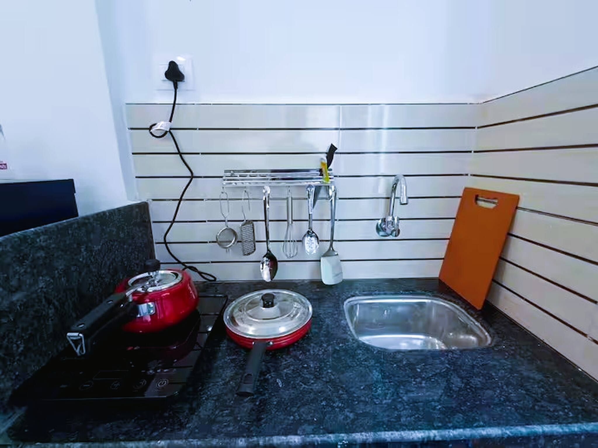 A kitchen with a stove, a sink, and utensils hanging on the wall.