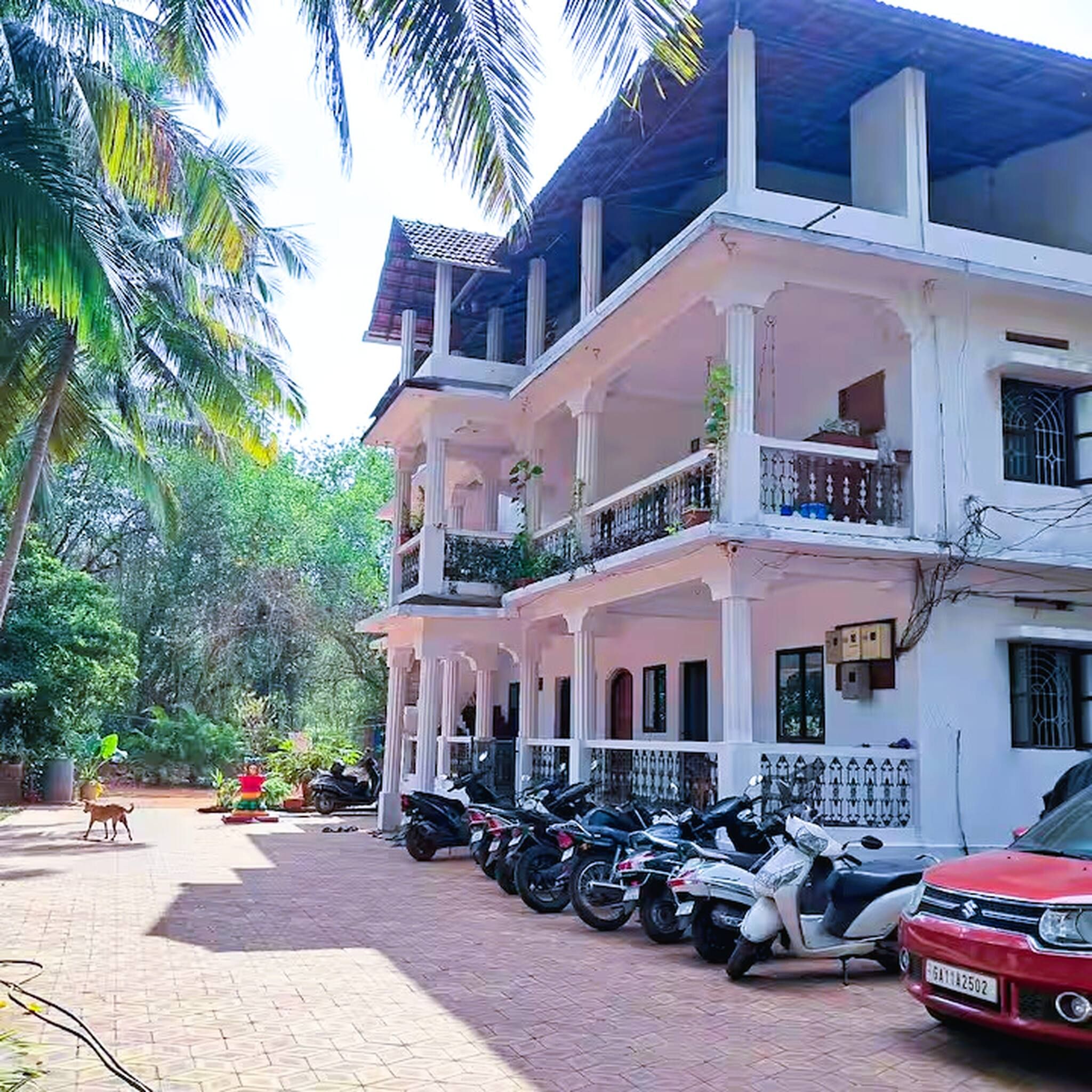 A multi-story building with a balcony, parked motorcycles, and a red car.