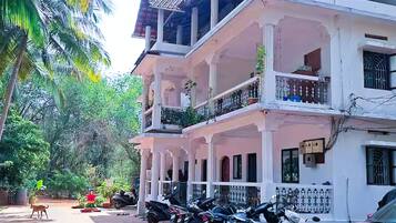A multi-story building with a balcony, parked motorcycles, and a red car.