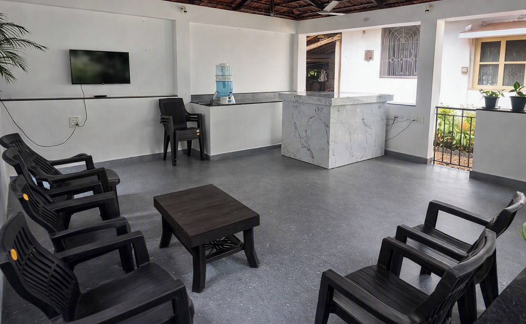 A modern interior with a seating area, a flat-screen TV, a water dispenser, and a balcony with plants.