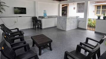 A modern interior with a seating area, a flat-screen TV, a water dispenser, and a balcony with plants.