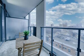 Ein Balkon mit Holztisch und -stühlen, einem Blumentopf und Blick auf die Stadt.