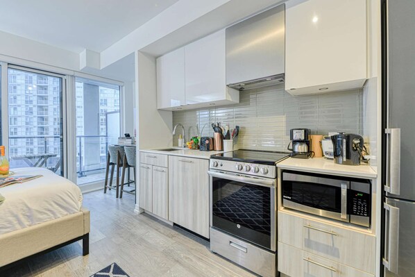 A modern kitchen with a stove, oven, microwave, and coffee maker. There is a dining area with a table and chairs.