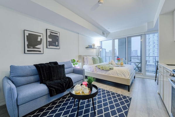 Ein modernes Schlafzimmer mit Bett, Sofa und Balkon mit Blick auf die Stadt.