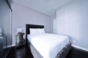 A modern hotel room with a large bed, a bedside table with a lamp, and a wardrobe. - RivetStays | The York Classic Suite – 1 Bedroom Condo (Toronto)