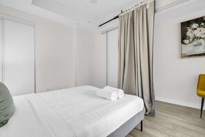 A modern hotel room with a neatly made bed, a chair, and a painting on the wall. - RivetStays | The Jarvis Deluxe Suite – 1 Bedroom Suite (Toronto)