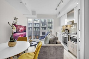 A modern apartment with a dining area, a sofa, a kitchen, and large windows offering a city view. - RivetStays | The Jarvis Deluxe Suite – 1 Bedroom Suite (Toronto)