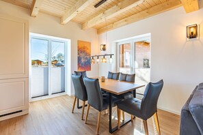 A modern dining area with a wooden table and chairs, large windows, and a view of the outside. - Ferienhaus mit Sauna und Whirlpool in Kating (Toenning)