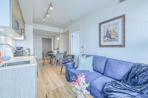 A modern living room with a blue sofa, a dining area with a table and chairs, and a kitchen with a sink and appliances. - RivetStays | The Jarvis Executive Suite – 2 Bedroom Suite (Toronto)