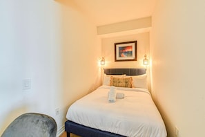 A hotel room with a bed, a headboard, a painting above the bed, and two wall-mounted lights. - RivetStays | The Jarvis Executive Suite – 2 Bedroom Suite (Toronto)