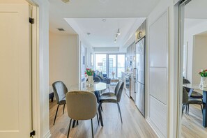 A modern kitchen with a large island, a dining area with a round table, and a view of the city through large windows. - RivetStays | The Jarvis Executive Suite – 2 Bedroom Suite (Toronto)