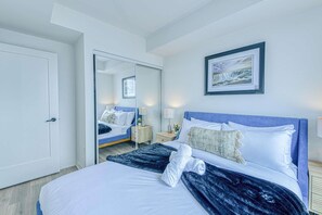 A modern hotel room with a large bed, a bedside table with a lamp, a mirror, and a framed picture on the wall. - RivetStays | The Jarvis Executive Suite – 2 Bedroom Suite (Toronto)