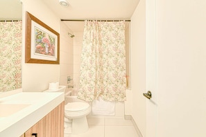 A bathroom with a shower curtain, toilet, and a framed picture on the wall. - RivetStays | The Jarvis Honeymoon Suite – Romantic 2 Bedroom Suite (Toronto)
