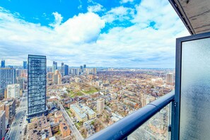A high-rise building with a modern glass facade, surrounded by a mix of residential and commercial buildings, viewed from a balcony with a clear sky. - RivetStays | The Jarvis Honeymoon Suite – Romantic 2 Bedroom Suite (Toronto)