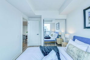 A modern hotel room with a large bed, a desk, and a view of the city through the window. - RivetStays | The Jarvis Honeymoon Suite – Romantic 2 Bedroom Suite (Toronto)