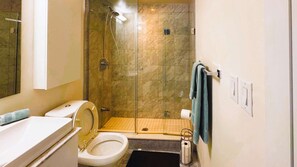 A bathroom with a toilet, a shower enclosure, a towel rack, and a toilet paper holder. - RivetStays | The York City Suite – Studio Condo (Toronto)