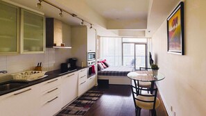 A compact kitchen with a microwave, coffee maker, and a small dining area with a table and chairs. - RivetStays | The York City Suite – Studio Condo (Toronto)