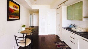 A modern kitchen with white cabinets, a glass dining table, and a painting on the wall. - RivetStays | The York City Suite – Studio Condo (Toronto)