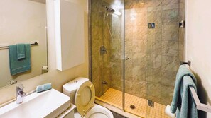 A bathroom with a toilet, sink, and glass-enclosed shower. - RivetStays | The York City Suite – Studio Condo (Toronto)