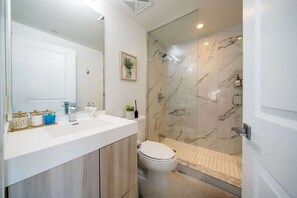 Une salle de bain moderne avec un meuble-lavabo blanc, une cabine de douche en verre et des toilettes.