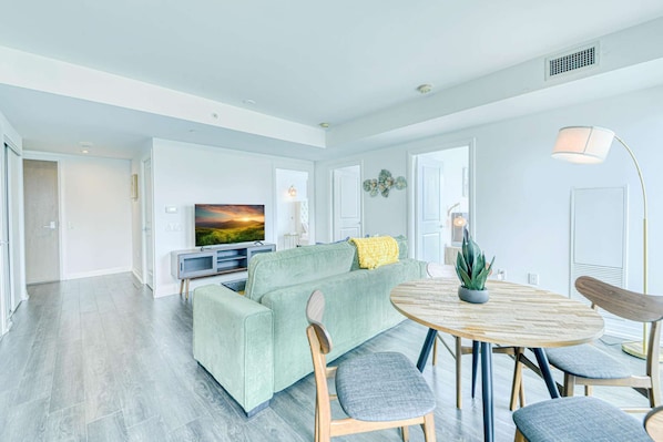 Un salon moderne avec un canapé, un téléviseur et une table ronde entourée de chaises.
