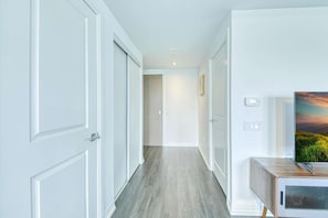 Un couloir avec des portes blanches, un plancher en bois, un téléviseur posé sur un meuble en bois et un thermostat fixé au mur.