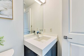 A modern bathroom with a white sink, a mirror, and a door. - RivetStays | The Jarvis Exclusive Suite – 3 Bedroom Condo (Toronto)