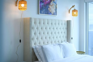 A bedroom with a tufted headboard, white bedding, and two wall-mounted lamps. - RivetStays | The Jarvis Exclusive Suite – 3 Bedroom Condo (Toronto)