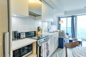 Une cuisine compacte équipée d’un four à micro-ondes, d’un grille-pain, d’une cuisinière et d’un évier. Un coin repas avec une chaise et une table est à disposition, ainsi qu’une grande fenêtre offrant une vue agréable.