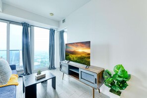 Un salon moderne avec une grande fenêtre, un téléviseur à écran plat, une table basse et une plante en pot.