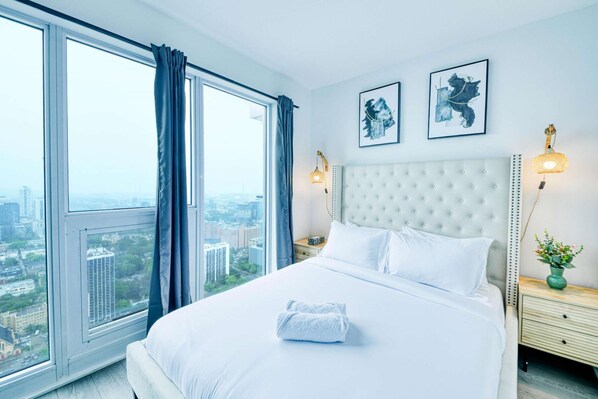 Une chambre d’hôtel moderne avec un grand lit, une vue sur la ville et deux œuvres d’art encadrées au mur.