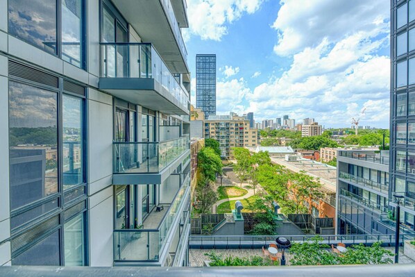 A modern building with large windows and a courtyard with greenery and seating areas. - RivetStays | The Jarvis Business Suite – Downtown Studio Suite (Toronto)