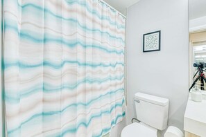 A bathroom with a striped shower curtain, a toilet, and a framed picture on the wall. - RivetStays | The Jarvis Business Suite – Downtown Studio Suite (Toronto)