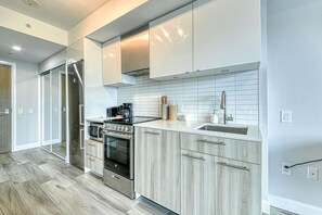 A modern kitchen with stainless steel appliances, light wood cabinetry, and a white tiled backsplash. - RivetStays | The Jarvis Business Suite – Downtown Studio Suite (Toronto)