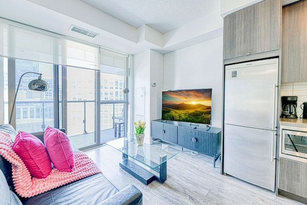 Een modern appartement met grote ramen, een flatscreen-tv, een koelkast en een glazen salontafel.
