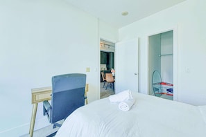 Een hotelkamer met een bed, een bureau met stoel, een badkamer met spiegel en een keuken zichtbaar door een open deur.