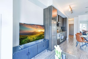 Een moderne keuken met een ingebouwde oven, een grote flatscreen televisie aan de muur en een eethoek met een glazen tafel en stoelen.
