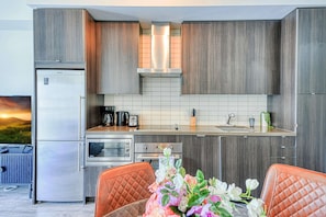 A modern kitchen with wooden cabinets, a stainless steel refrigerator, a microwave, and a toaster. There is a sink with a faucet, a countertop with a coffee maker, and a vase with flowers on the table. - The Atmos by RivetStays – Cozy 1BR in the Heart of Toronto (Toronto)
