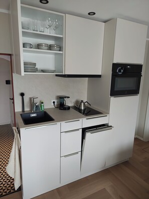 A compact kitchen with white cabinets, a built-in oven, a sink, and a countertop with a kettle and a coffee maker. - Elbhangsauna - Vacation Rental with Private Sauna and View of the Elbe River (Pirna)