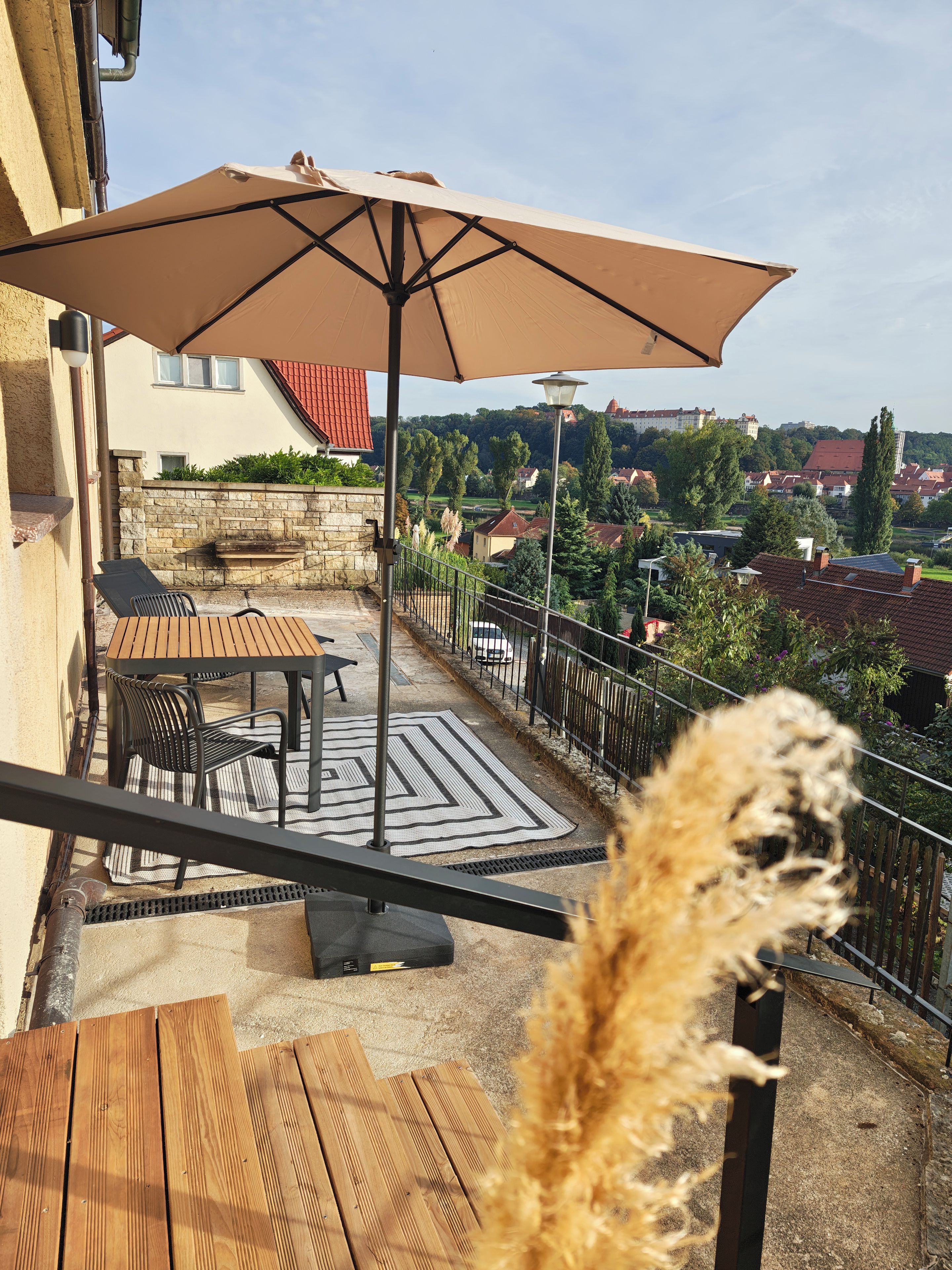 Un balcon avec une table et des chaises, un parasol et une vue sur la ville.