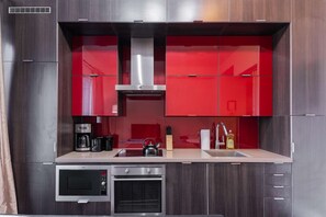 A modern kitchen with red cabinets, a built-in oven, a coffee maker, and a kettle. - RivetStays | The Atmos Deluxe 2 Suite – 1 Bedroom Suite (Toronto)