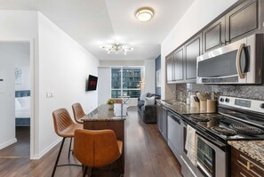 A modern kitchen with a central island, stainless steel appliances, and a view to the outside. - RivetStays | The Neptune Signature Suite – 1 Bedroom + Den Condo (Toronto)
