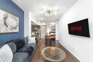 A modern living room with a grey sofa, a glass coffee table, and a flat-screen TV displaying 'NETFLIX'. - RivetStays | The Neptune Signature Suite – 1 Bedroom + Den Condo (Toronto)