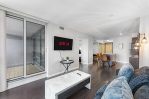 A modern living room with a flat-screen TV mounted on the wall, a coffee table, and a sofa. - RivetStays | The Neptune Design Suite – 1 Bedroom + Den Condo (Toronto)