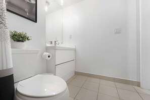 A bathroom with a toilet, a sink, and a mirror. - RivetStays | The Neptune Design Suite – 1 Bedroom + Den Condo (Toronto)