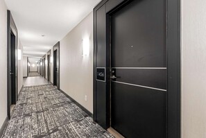 A hotel hallway with a carpeted floor, a black door with a number plate, and a series of doors along the corridor. - RivetStays | The Neptune Design Suite – 1 Bedroom + Den Condo (Toronto)