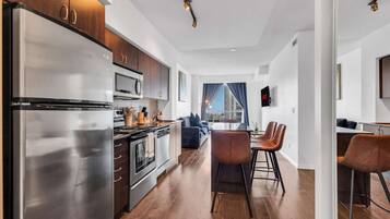 A modern kitchen with stainless steel appliances, a dining area with bar stools, and a view of the cityscape through large windows.