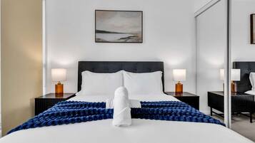 A hotel room with a large bed, two bedside tables with lamps, a wall-mounted painting, and a mirror.
