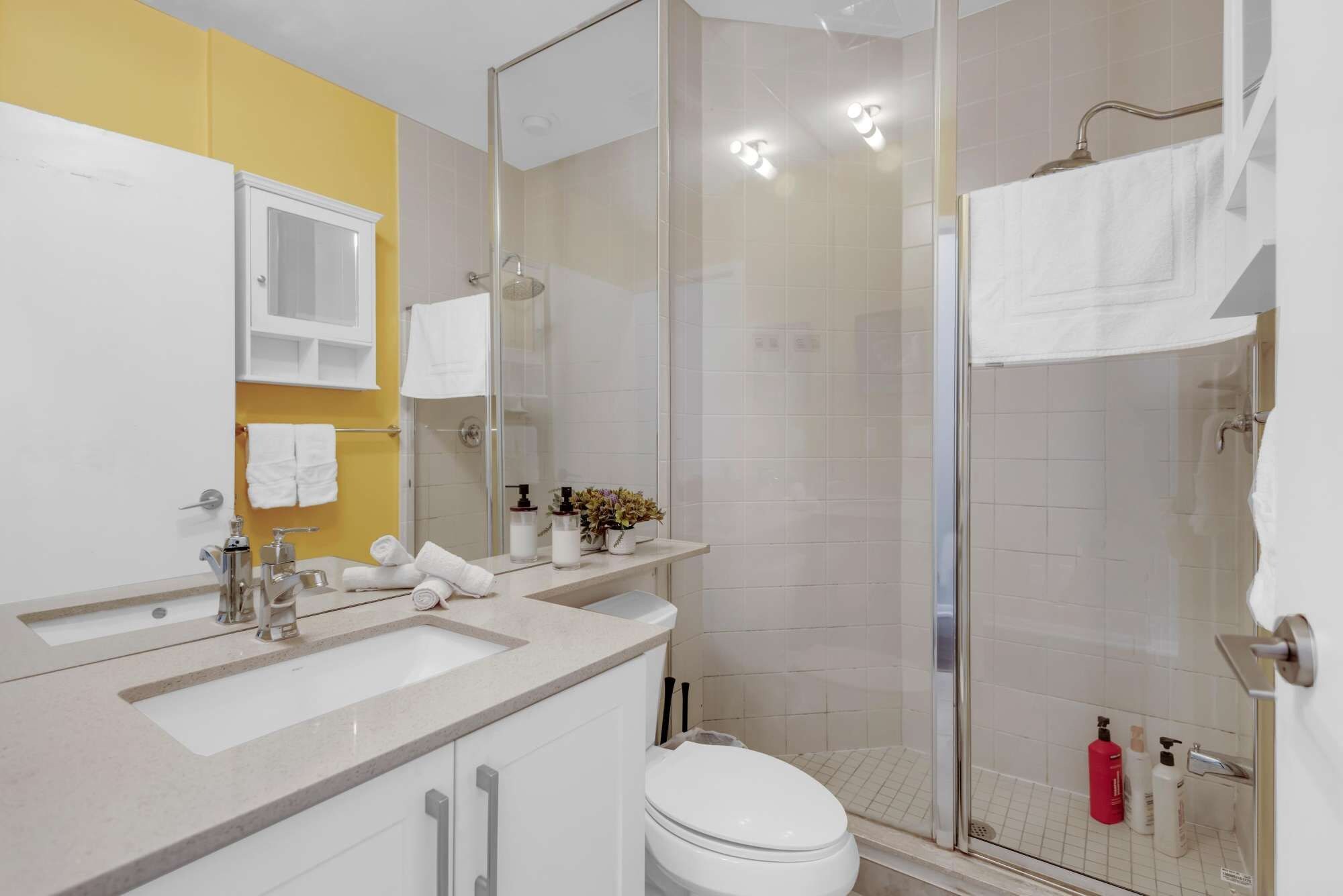 A modern bathroom with a glass shower enclosure, a white toilet, and a vanity with a sink and mirror.
